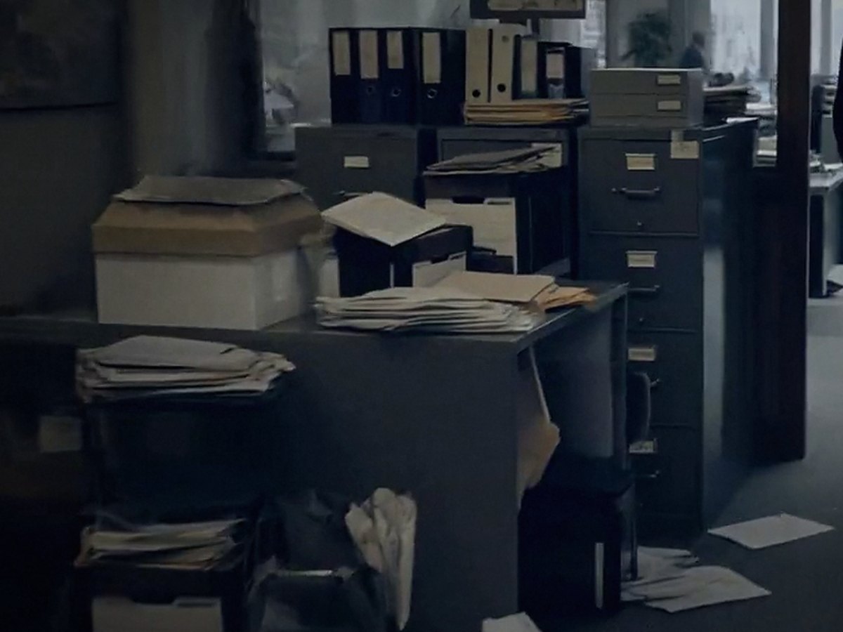 A cramped office with paperwork stacked on every surface and papers across the floor